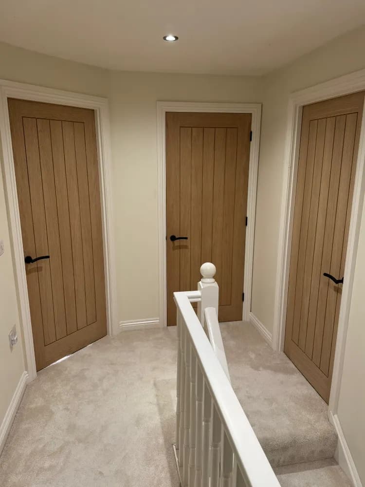 Three oak ledged internal doors fitted on a landing beside a white staircase balustrade